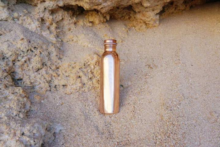 Copper H2O smooth copper water bottle placed on sand