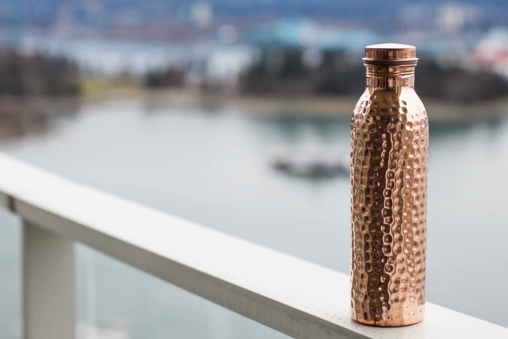 Copper H2O hammered copper water bottle placed on a railing
