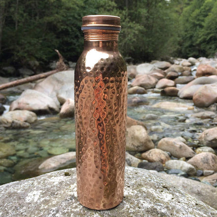 Close up of a copper water bottle on a rock with a river behind