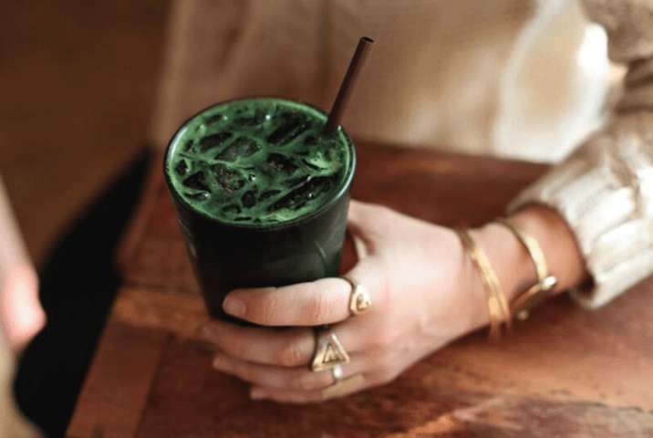 hand wearing gold rings resting on table holding green drink