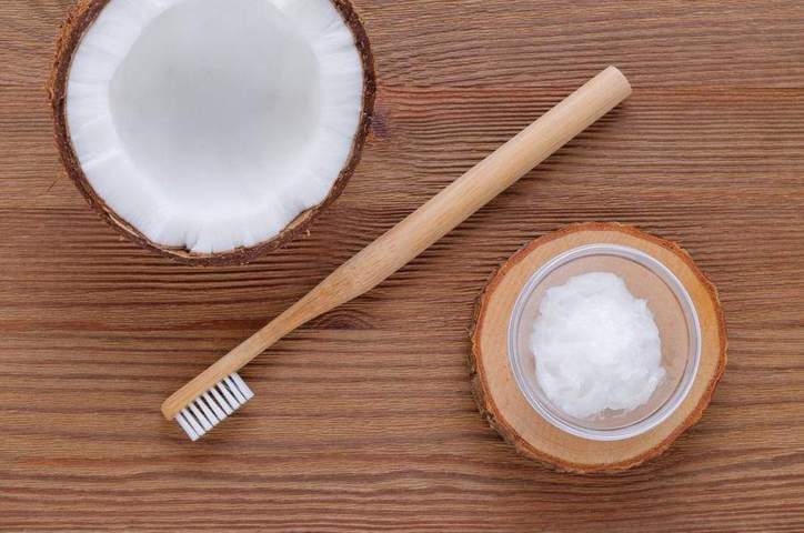 half open coconut hush wooden toothbrush small jar filled with coconut oil placed on a wooden surface top view