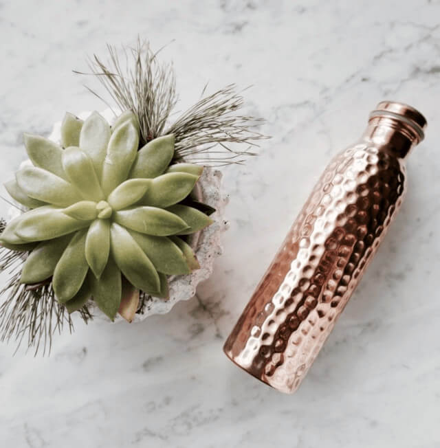 Copper H2O hammered copper water bottled placed on marble surface beside succulent plant