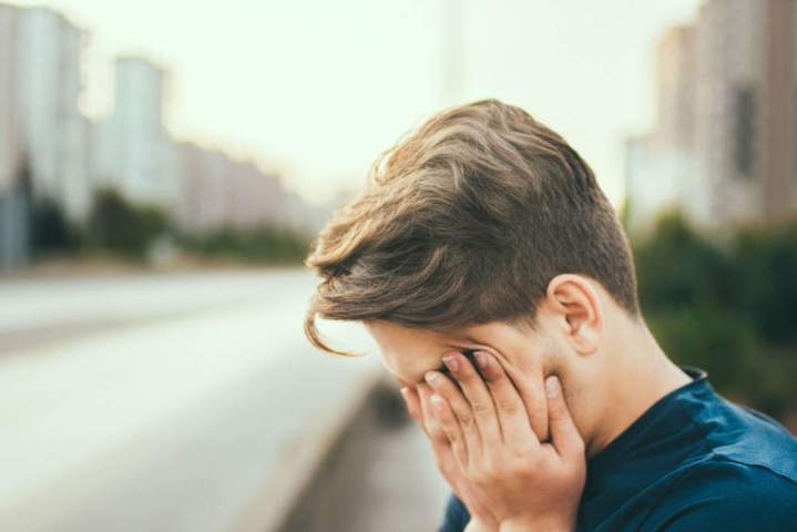 boy covering his face with his hands blurry city background