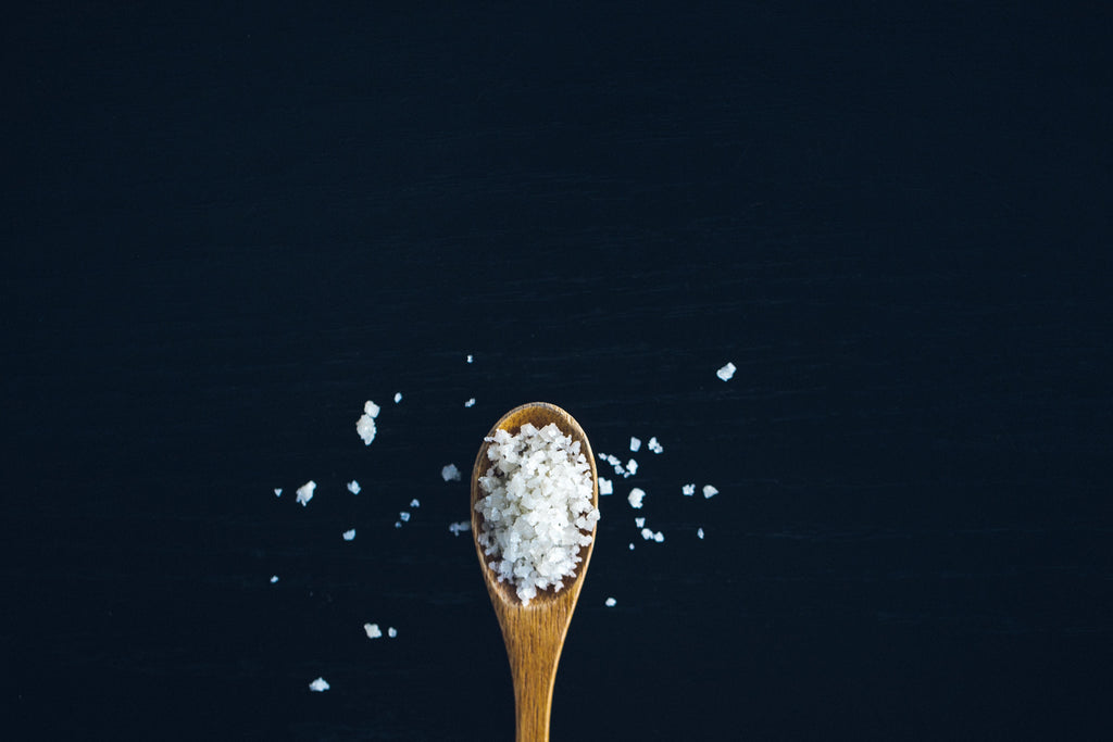 wooden spoon filled with salt placed on a black background