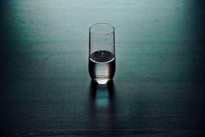 half filled glass of water wooden surface dark background
