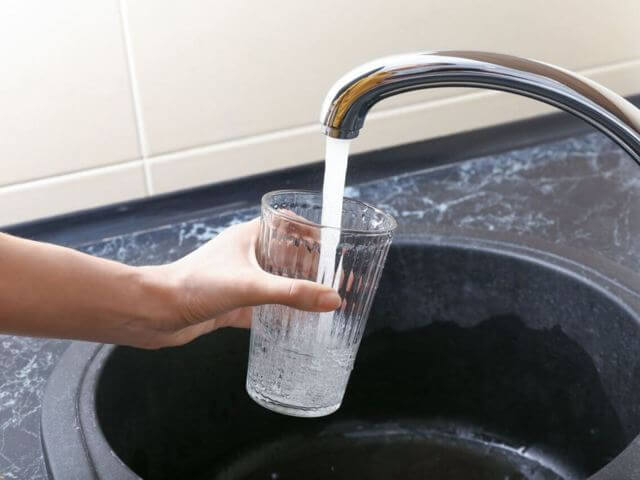 hand holding glass filling water from faucet black sink